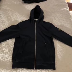 Marine blå windbraker från Stone Island - Säljer en marine blå windbreaker från Stone Island i mycket bra skick. Den har en dragkedja framtill och en klassisk logga på ärmen. Perfekt för höst och vår, med en stilren och bekväm design. Passar både till vardags och lite mer avslappnade tillfällen. Den är i stl 156 dvs 12a skulle säga 8/10 skick den har ett litet skrap märke på ryggen. Pris går att diskuteras