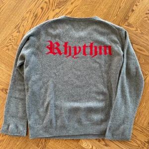 Grå kashmirtröja från Zadig & Voltaire - Säljer en helt ny, supermjuk och stilren grå tröja från Zadig & Voltaire i kashmir och ull. Den har ett coolt rött 'Rhythm'-tryck på ryggen. Perfekt för både höst och vinter, med långa ärmar och ribbade kanter. Passar perfekt för en avslappnad men ändå trendig look. Storlek herr M, passar även L