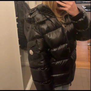  Moncler jacka  - Säljer en snygg svart pufferjacka från Moncler i mycket bra skick. Jackan är perfekt för vintern med sitt varma dunfoder och har en cool glansig finish. Den har en dragkedja framtill och Monclers logga på ärmen. Passar perfekt för kalla dagar och ger en stilren look. Size small- large min brud provar small o medium passar för både tjejer och killar 