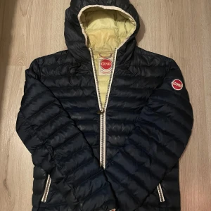 Svart pufferjacka från Colmar - Säljer en snygg svart pufferjacka från Colmar i använt skick. Har inga synliga defekter förutom inuti jackan där det är lite missfärgning. Jackan har en dragkedja fram och en mysig huva. Insidan är beige och ger en cool kontrast. Perfekt för höst och vinter! 🖤