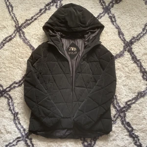 Svart quiltad jacka från Zara - Säljer en svart quiltad jacka från Zara i storlek 164. Jackan har en mysig huva och stängs med dragkedja. Perfekt för höst och vinter med sin varma och stilrena design. Den är i mycket bra skick och säljer den för 190+frakt.