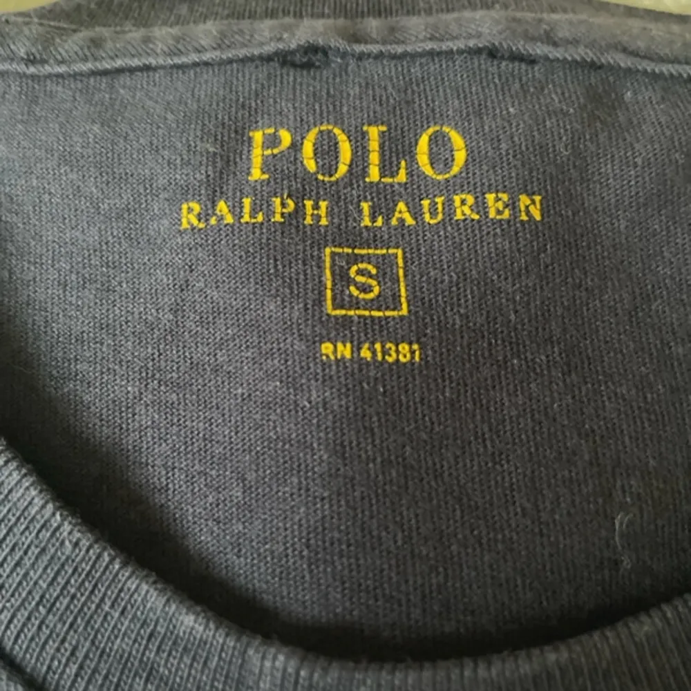 Säljer en snygg mörkblå t-shirt från Ralph Lauren i storlek S. Den har en klassisk design med en röd broderad logga på bröstet. Perfekt för en stilren och avslappnad look. T-shirten är i mycket bra skick och gjord av mjukt bomullsmaterial.. T-shirts.