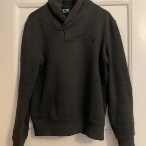 Mörkgrå tröja från Polo Ralph Lauren - Säljer en stilren mörkgrå tröja från Polo Ralph Lauren i storlek S. Tröjan har en snygg krage med knappdetalj och är perfekt för både vardag och lite finare tillfällen. Den är i mycket bra skick och passar perfekt till höst och vinter. 🖤