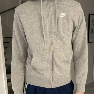 Säljer en grå hoodie från Nike i bra skick. Blivit missfärgad inuti, så det är en lite rosa ton. Den har en dragkedja framtill och en klassisk huva. Perfekt för både träning och vardag. Storleken är normal och materialet känns mjukt och bekvämt. Passar till alla säsonger!