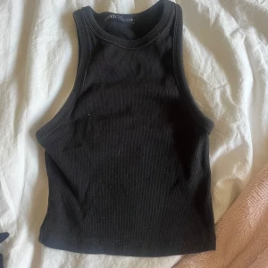 Svart ribbad linnetopp - Säljer en svart ribbad linnetopp från zara i storlek S. Toppen är ärmlös och har en tight passform, perfekt för sommardagar eller som ett basplagg i garderoben. Den är i mycket bra skick och redo för en ny ägare!