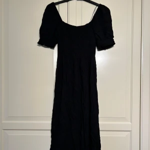 Svart klänning från H&M - Säljer en svart långklänning från H&M i storlek XS. Klänningen har korta puffärmar och en resor överdel som ger en fin passform. Perfekt för både vardag och festliga tillfällen!