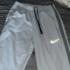 Grå träningsbyxor från Nike - Säljer ett par grå träningsbyxor från Nike i Dri-FIT material. De har en elastisk midja med snörning och en reflekterande Nike-logga på benet. Perfekta för träning eller en avslappnad dag. 🏃‍♂️ dom är som helt nya inte ens använda en gång