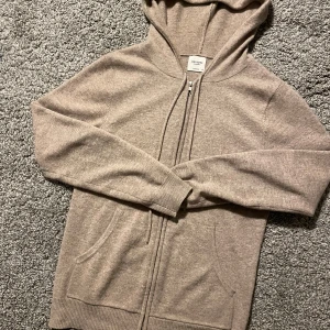 Beige cashmere hoodie från John Henric - Säljer en supermjuk och lyxig beige hoodie i 100% cashmere från John Henric. Perfekt för kyliga dagar med sin dragkedja och bekväma passform. Den har långa ärmar och en praktisk huva. Ett måste för garderoben! 🧥✨
