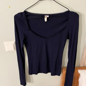 Mörkblå topp från Nelly - Säljer en mörkblå långärmad topp från Nelly i storlek XS. Toppen har en v-ringad design med spetsdetaljer längs halsringningen. Perfekt för både vardag och fest!