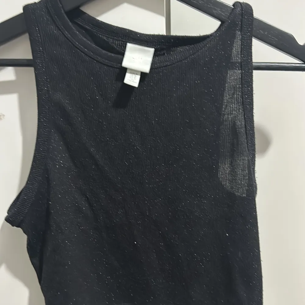 Snygg svart ärmlös topp från H&M med glittrande detaljer. Perfekt för en utekväll eller fest! Toppen är ribbad och har en tight passform som framhäver figuren. Ett måste i garderoben för alla som älskar att glittra!. Yläosat.