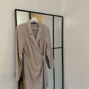 Beige omlottklänning från Gina Tricot - Säljer en elegant beige omlottklänning från Gina Tricot. Klänningen har långa ärmar och en stilren design med knytning i midjan. Perfekt för både vardag och festliga tillfällen. Passar bra till höst och vår! Fin passform och ramar in kroppen fint men den blir för aningen för kort (för min del) att använda som klänning. Därav anledningen till att jag säljer den. Har aldrig hunnit använda kavajklänningen, prislappen är dock inte kvar. Tillverkad i 93% polyester och 7% elastan. 🧡