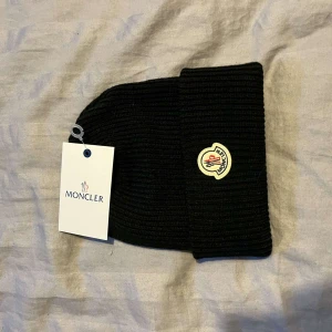  mössa från Moncler - Säljer en snygg svart ribbad mössa från Moncler. Den är i nytt skick och har en broderad Moncler-logga framtill. Perfekt för att hålla sig varm och stilren under de kallare månaderna. Passar till alla outfits!