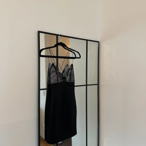 Svart klänning med spetsdetaljer - Säljer en elegant svart klänning med vackra spetsdetaljer vid bysten. Klänningen har tunna axelband och en figurnära passform, perfekt för festliga tillfällen. Den är i mycket bra skick och redo att bäras på nästa fest! Har aldrig använt, dock är prislappen  borttagen. Säljer den eftersom den är för liten för mig och den bara hängt i garderoben senaste året. Tillverkad i 89% polyester, 11% elastan. 🖤