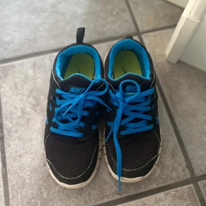 Svarta Nike sneakers med blå detaljer - Säljer ett par svarta Nike sneakers med blå snörning och detaljer!