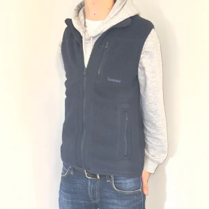 Blå fleeceväst, Timberland - Säljer en snygg svart fleeceväst från Timberland i mycket bra skick. Västen har dragkedja framtill och två praktiska fickor med dragkedjor. Perfekt för lager-på-lager under höst och vår. Passar både till vardags och för utomhusaktiviteter.