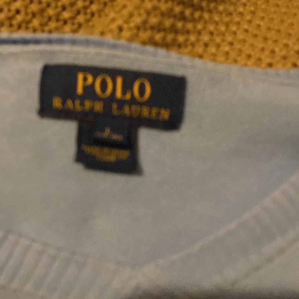 Säljer en snygg ljusblå tröja från Polo Ralph Lauren. Den har en klassisk v-ringning och är prydd med det ikoniska gula broderade logotypen på bröstet. Perfekt för både vardag och lite finare tillfällen. Passar bra till jeans eller chinos!. Tröjor & Koftor.