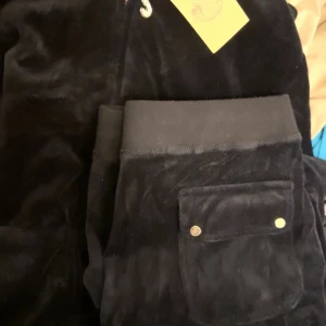 Svarta mjukisbyxor i sammet - Säljer ett par svarta mjukisbyxor i sammet. De har en bekväm passform med elastisk midja och en praktisk ficka med knappdetalj. Perfekta för mysiga dagar hemma eller en avslappnad dag ute.