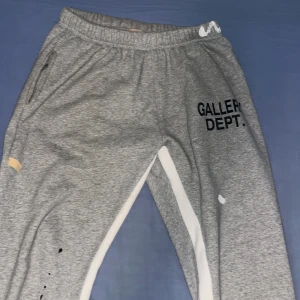Grå mjukisbyxor från Gallery Dept. - Säljer ett par grå mjukisbyxor från Gallery Dept. i storlek L. Byxorna är tillverkade i 100% bomull och har en avslappnad stil med elastisk midja. De har coola färgstänk och tryckdetaljer som ger en unik look. Perfekta för en casual och bekväm stil!