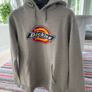 Grå hoodie från Dickies - Säljer en grå hoodie från Dickies i använt skick. Loggan på bröstet är komplett men har små sprickor . Perfekt för vardagsbruk eller chill dagar hemma.
