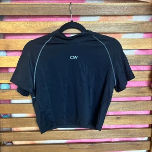 Träningstopp: ICANIWILL - Säljer en svart kortärmad träningstopp från ICANIWILL. Toppen har en tight passform och är perfekt för träning. Den är gjord i ett syntetmaterial som andas och har snygga kontrastsömmar. Perfekt för gymmet eller löprundan!