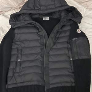 Säljer en snygg svart jacka från Moncler. Den har en quiltad design med dragkedja och en praktisk huva. Perfekt för höst och vinter. Jackan har långa ärmar och en liten ficka med dragkedja på ärmen. Superbra skick och redo för nya äventyr!