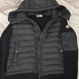 Svart jacka från Moncler - Säljer en snygg svart jacka från Moncler. Den har en quiltad design med dragkedja och en praktisk huva. Perfekt för höst och vinter. Jackan har långa ärmar och en liten ficka med dragkedja på ärmen. Superbra skick och redo för nya äventyr!