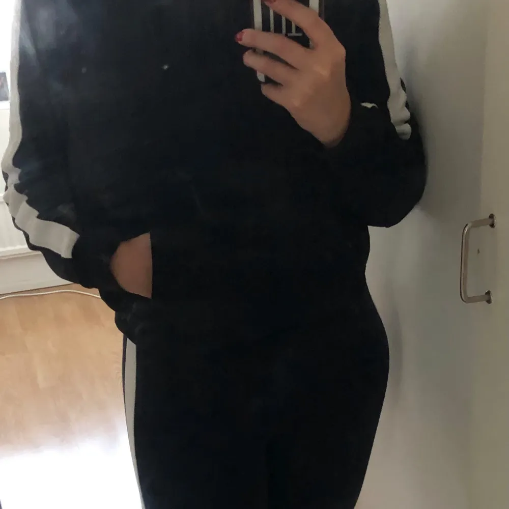 Säljer en svart hoodie med vita ränder längs ärmarna samt matchande leggings. Hoodien har en huva och fickor framtill, perfekt för träning eller en avslappnad dag. Den är i bra skick och superbekväm att ha på sig. Passar perfekt till höst och vår!. Hoodies.