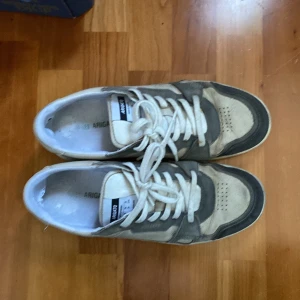 Sneakers från Axel Arigato - Säljer ett par stilrena sneakers från Axel Arigato i beige och grått. Skorna har snörning och en klassisk design med märkets logga på sulan. Perfekta för både vardag och fest! De är i bra skick med lite slitage på sulan. Säljer billigt pågrund av skicket, kan tänka mig att gå ner i pris
