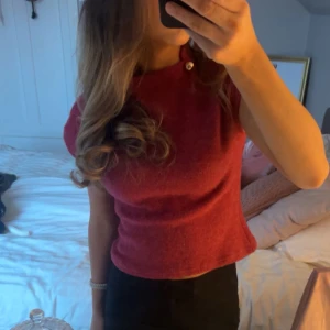 Röd kortärmad topp med knappdetalj - Säljer en snygg röd  stickad topp med korta ärmar och en fin knappdetalj vid halsen. ❣️❣️