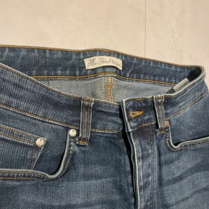 Blå jeans från The Blue Uniform  - Säljer ett par snygga blå jeans från The Blue Uniform. De har en klassisk femficksdesign och är i bra skick. Perfekta för vardagsbruk med en skön passform. De har en dragkedja och knapp framtill.