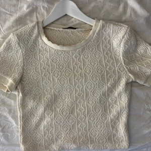 Vit stickad topp från Zara - Säljer en söt vit stickad topp från Zara. Den har ett fint mönster och korta ärmar, perfekt för vår och sommar. Toppen är i bra skick och passar både till vardags och fest. Superfin att matcha med jeans eller kjol!