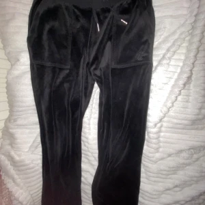 Svarta mjukisbyxor från Juicy Couture - Säljer ett par svarta mjukisbyxor från Juicy Couture i storlek 12/13. De är supermjuka och har en snygg glansig finish. Byxorna har snörning i midjan och bakfickor med knappar. Mest använda hemma och köptes förra året, nu inte super mycket till användning för mig. De tvättas och packas innan de kommer fram. Skriv vid intresse