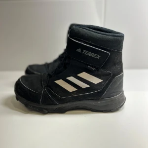 Svarta Terrex vinterboots från Adidas - Säljer ett par svarta Terrex vinterboots från Adidas i bra skick, storlek 37 och 1/3. De är mycket bekväma och har en robust sula perfekt för utomhusaktiviteter. Perfekta för vinteräventyr!