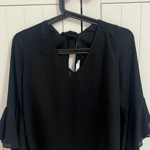 Svart blus - Superfin svart blus med öppen rygg från NA-KD i storlek 36, men passar även storlek 34. Den har bara använts en gång och är i mycket gott skick. Elegant och mångsidig en perfekt blus för många tillfällen!