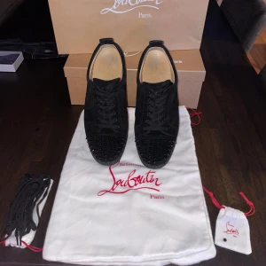 Svarta sneakers med nitar från Christian Louboutin - Säljer ett par svarta sneakers från Christian Louboutin i mycket bra skick. Påsarna, niten, skosnörena och skokartongen ingår. Storlek 41 1/2, passar 42. Skorna säljes pga att dem inte används mer. Kvitto finns vid köp av vara.