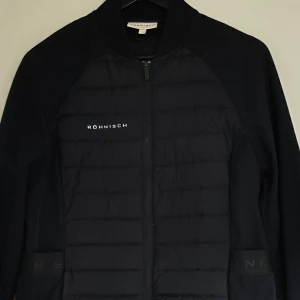 Svart jacka från Röhnisch - Säljer en snygg svart jacka från Röhnisch. Den har en quiltad design framtill och dragkedja. Perfekt för kyliga dagar och passar bra till både vardag och träning. Jackan har långa ärmar och en stilren look.