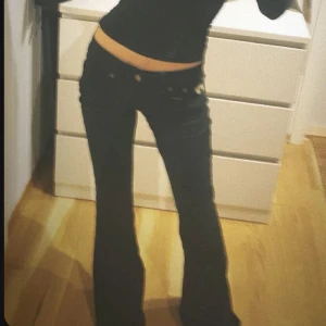 Svarta bootcut jeans - Säljer ett par snygga svarta bootcut jeans i bra skick. De är lågmidjade och har en klassisk femficksdesign med knappar och dragkedja. Perfekta för både vardag och fest! 🖤