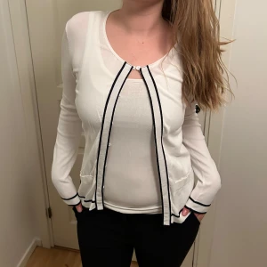 Vit kofta med svarta detaljer - Säljer en stilren vit kofta med svarta kantdetaljer. Den har knappar framtill och två små fickor. Perfekt för både vardag och fest! 🖤