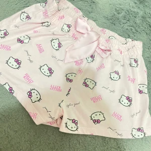 Rosa Hello Kitty shorts - Supergulliga rosa shorts med Hello Kitty-motiv över hela tyget. De har en söt rosett i midjan och är perfekta för en avslappnad dag hemma. Materialet känns mjukt och bekvämt, och den elastiska midjan gör dem lätta att bära. Perfekta för alla Hello Kitty-fans! Står storlek XL L men passar bara XS S