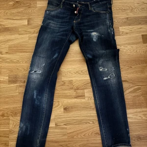 Mörkblå jeans från Dsquared2 - Säljer ett par snygga mörkblå jeans från Dsquared2 i storlek 48. De har en cool slitningseffekt och är i bra skick. Perfekta för en casual look eller en utekväll. Passformen är slim. Ny pris runt 4000kr