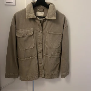 Beige jacka från Pull&Bear - Säljer en snygg beige jacka från Pull&Bear i storlek S. Jackan har en avslappnad stil med stora fickor och knappar framtill. Perfekt för höst och vår, och den är i mycket bra skick. Passar både till vardags och lite mer uppklädda tillfällen.