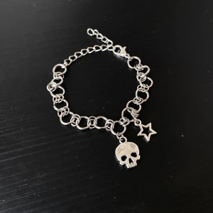 Handgjort Silverfärgat armband med dödskalle och stjärna - Coolt armband i silverfärg med en kedja av sammanlänkade ringar. Den är ca 16 cm men kan justeras upp till 20 cm. Det har två hängande berlocker: en detaljerad dödskalle och en stjärna. Perfekt för att ge din outfit en edgy touch. Passar både till vardags och fest!