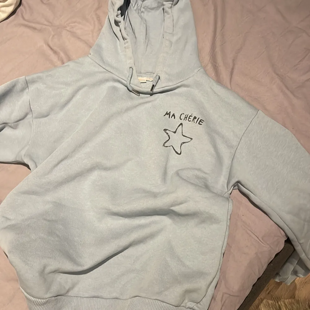 Säljer en supermysig grå hoodie från Gina Tricot med texten 'Ma Chérie' och en stjärna på framsidan. Perfekt för chilliga dagar eller när du vill vara bekväm men ändå snygg. Den har en klassisk huva och ribbade muddar. Passar perfekt till jeans eller leggings! Liten i storleken då de är storlek 166/152 säljer för 250. Tröjor & Koftor.