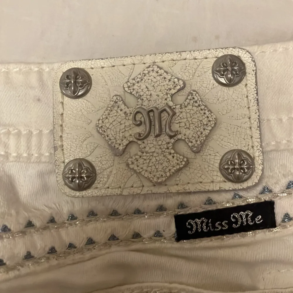 Säljer ett par vita jeans från Miss Me i storlek 26. De har snygga silverknappar och dekorativa detaljer med broderi och nitar på fickorna. Perfekta för en stilren look med lite edge. Passar både till vardags och fest!. Farkut & Housut.