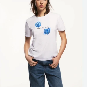 Vit t-shirt med blått tryck - Snygg vit t-shirt med blått tryck och texten 'Costa Amalfitana'. I storlek S.