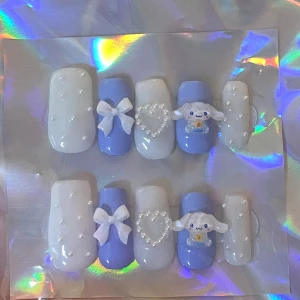 Söta Sanrio naglar med pärlor och rosetter - Supergulliga lösnaglar i blått och vitt med 3D-detaljer. De har små pärlor, rosetter och en söt figur på några av naglarna. Perfekt för en söt look eller speciella tillfällen! 💙✨