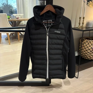  McKenzie cardigan  - Säljer en svart cardigan från McKenzie i ny  skick. Den har en dragkedja framtill och en huva för extra skydd mot väder. Perfekt för höst och vinter, med en stilren design som passar till det mesta. Jackan är långärmad och har en normal passform.