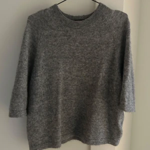 Grå stickad tshirt från & Other Stories - Mysig grå tröja från & Other Stories i storlek M. Perfekt för kyliga dagar med sin mjuka och varma känsla. Tröjan har trekvartsärmar och en klassisk rund halsringning. Passar både till vardags och lite finare tillfällen.