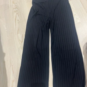 Svarta ribbade byxor från NAKD - Säljer ett par svarta ribbade byxor från NAKD i storlek S. De har en loose fit och är perfekta för både vardag och fest. Byxorna är högmidjade och gjorda i ett mjukt och bekvämt material. Passar perfekt till höst- och vintergarderoben!
