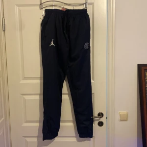 Svarta träningsbyxor från Jordan x PSG - Säljer ett par svarta träningsbyxor från Jordan x PSG i storlek L. Byxorna har elastisk midja och är dekorerade med Jordan-loggan och texten 'PARIS' längs benet. Perfekta för träning eller en avslappnad stil. 🖤